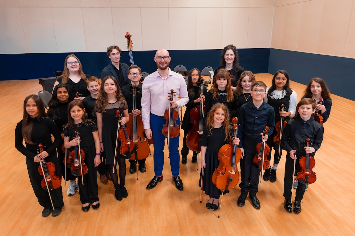 The junior ensemble — young string musicians ages 6 to 15 posing with their instruments.